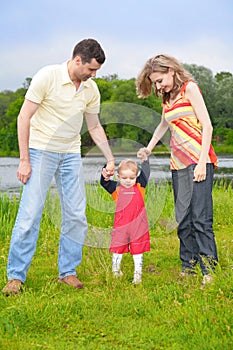 Parents hold for hands of child going on grass