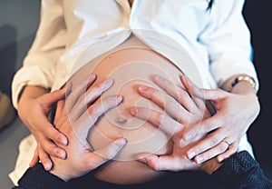 Parents holding hands on pregnant belly, loving the baby. Maternity concept