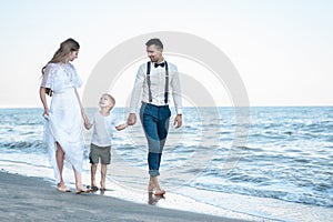 Parents holding hands of son and walking on beach. Beautiful couple with baby on the sea