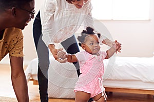 Parents At Home Encouraging Baby Daughter To Take First Steps