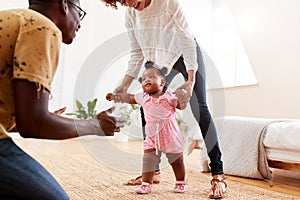 Parents At Home Encouraging Baby Daughter To Take First Steps