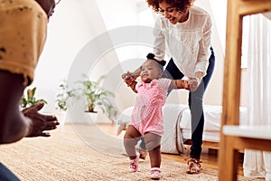 Parents At Home Encouraging Baby Daughter To Take First Steps