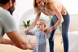 Parents At Home Encouraging Baby Son To Take First Steps