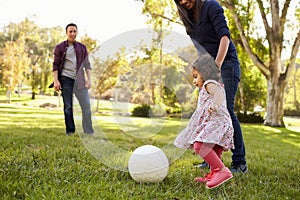 Parents kicking a ball with their young daughter in a park