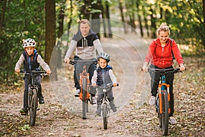 Parents and kids cycling on forest trail. family in warm clothes cycling autumn park. Family mountain bike on forest. active