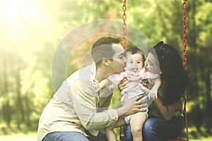 Parents kiss their child on swing