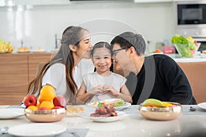 Parents kissing daughter at dinning table in kitchen