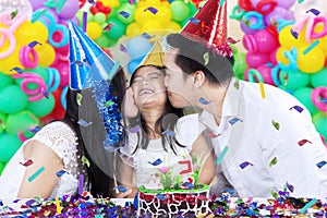 Parents kissing their child in birthday party