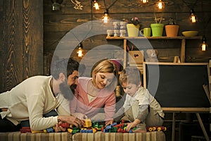 Parents lean forward to their kid on sofa. Family play with construction blocks. Dad looking at his busy son