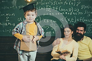 Parents listening their son, checking mistakes with book chalkboard on background. Boy presenting his knowledge to mom