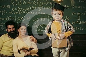 Parents listening their son, checking mistakes with book chalkboard on background. Boy presenting his knowledge to mom