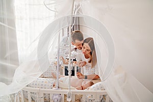 parents near a baby lies in a white crib with canopy