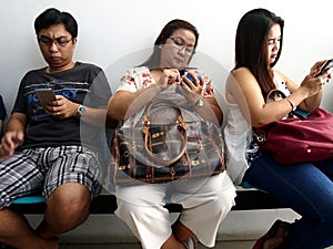 Parents play and work on their smartphones at a waiting area outside of their children`s class.