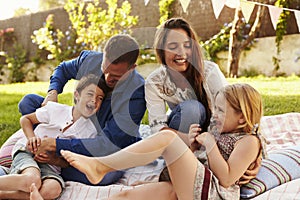 Parents Playing Game With Children On Blanket In Garden