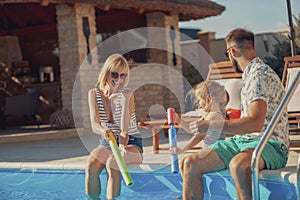 Parents playing with their daughter by the swimming pool, splashing water on each other