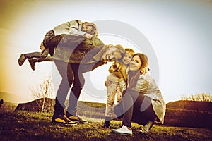 Parents playing with their daughters in the park. Father carryin