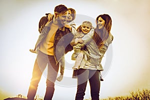 Parents playing with their daughters in the park. Father carrying his daughters on piggyback.