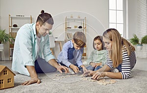 Parents playing with two kids in a puzzle on the floor in the living room at home.