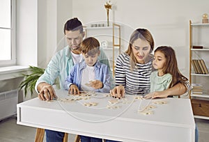 Parents playing with two kids in a puzzle in the living room at home.