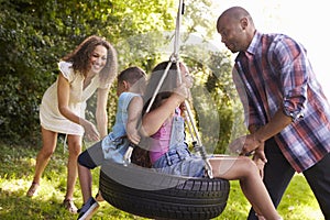 Parents Pushing Children On Tire Swing In Garden