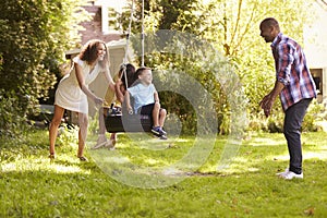 Parents Pushing Children On Tire Swing In Garden