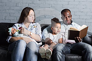 Parents read a book to children sitting on the couch. Happy multiethnic family. Family values