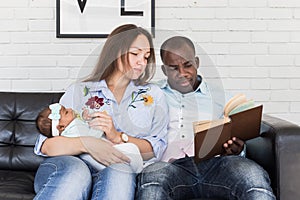 Parents read a book to children sitting on the couch. Happy multiethnic family. Family values