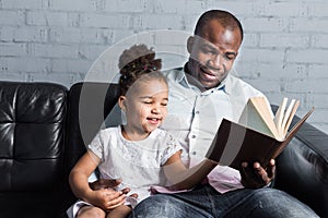 Parents read a book to children sitting on the couch. Happy multiethnic family. Family values