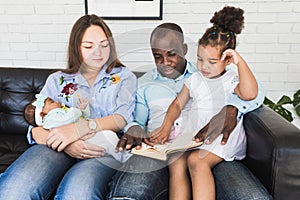 Parents read a book to children sitting on the couch. Happy multiethnic family. Family values