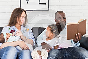 Parents read a book to children sitting on the couch. Happy multiethnic family. Family values