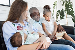 Parents read a book to children sitting on the couch. Happy multiethnic family. Family values