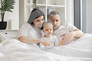 Parents reading baby book with daughter in bed at home