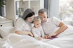 Parents reading baby book with daughter in bed at home