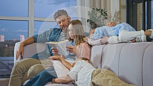 Parents reading book while children sleeping on sofa.