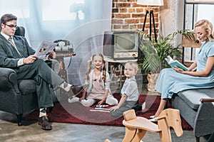 parents reading book and newspaper while kids playing with dominoes and smiling at camera