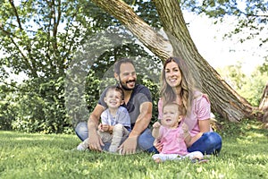 Parents Sitting With Children In Field close to a tree