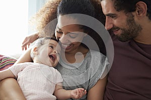 Parents Sitting On Sofa Cuddling Baby Daughter At Home