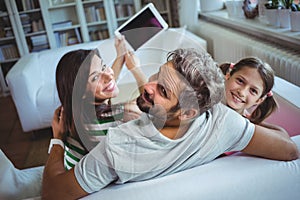 Parents sitting on sofa with daughter and clicking a selfie on digital tablet photo