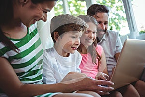 Parents sitting on sofa with their children and using laptop in living room