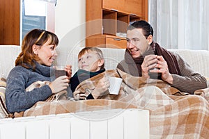 Parents and son warming near warm heater