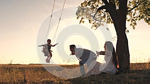 Parents swing the little girl on a swing on a summer day, flying like an airplane in the sky, happy mother and father