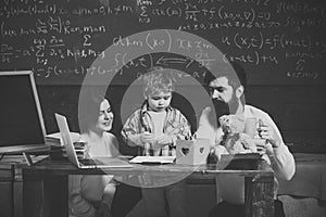 Parents teaches son, chalkboard on background. Boy listening to mom and dad with attention. Family cares about education
