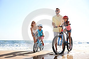 Parents teaching children to ride bicycles on sandy beach near sea