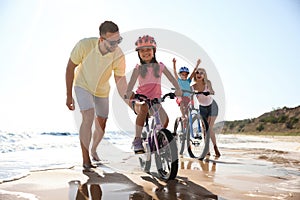 Parents teaching children to ride bicycles on sandy beach near sea