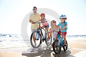 Parents teaching children to ride bicycles on sandy beach near sea