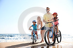 Parents teaching children to ride bicycles on sandy beach near sea