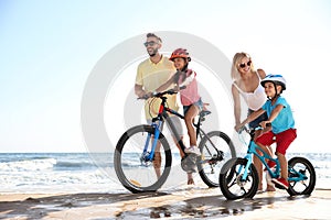 Parents teaching children to ride bicycles on sandy beach near sea