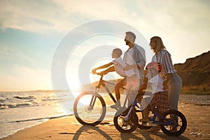 Parents teaching children to ride bicycles on sandy beach near sea at sunset