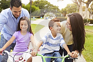 Parents Teaching Children To Ride Bikes In Park