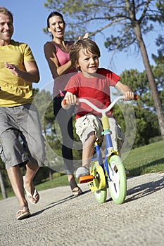 Parents Teaching Son To Ride Bike In Park